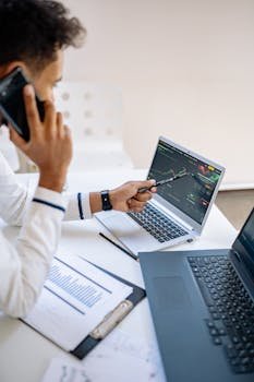 Business professional analyzing stock market data on laptops while on a phone call.